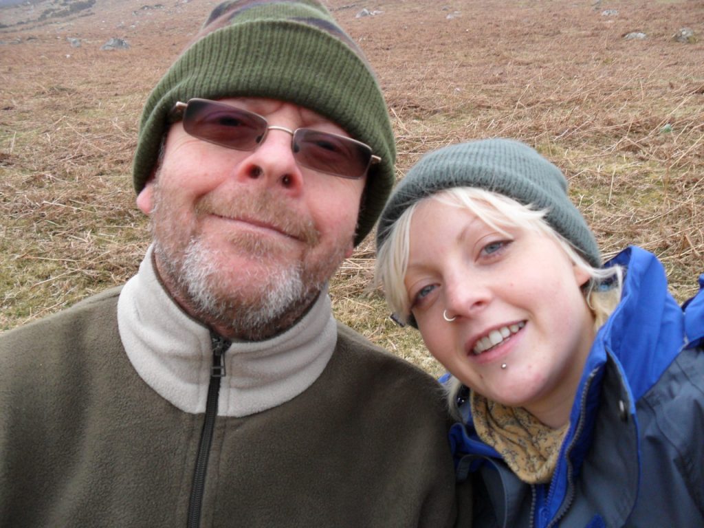 Rachael and her dad smiling together in woolly hats at the top of a mountain