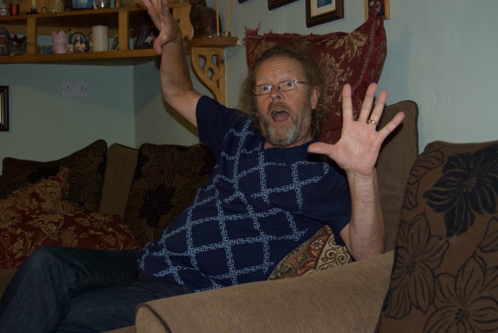 Rachael's dad sitting on the sofa at home, waving his hands with a playful expression